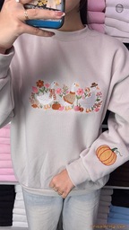 Model wearing an oversized light gray sweatshirt with embroidered ducks on the chest and a pumpkin print on the sleeve indoors.