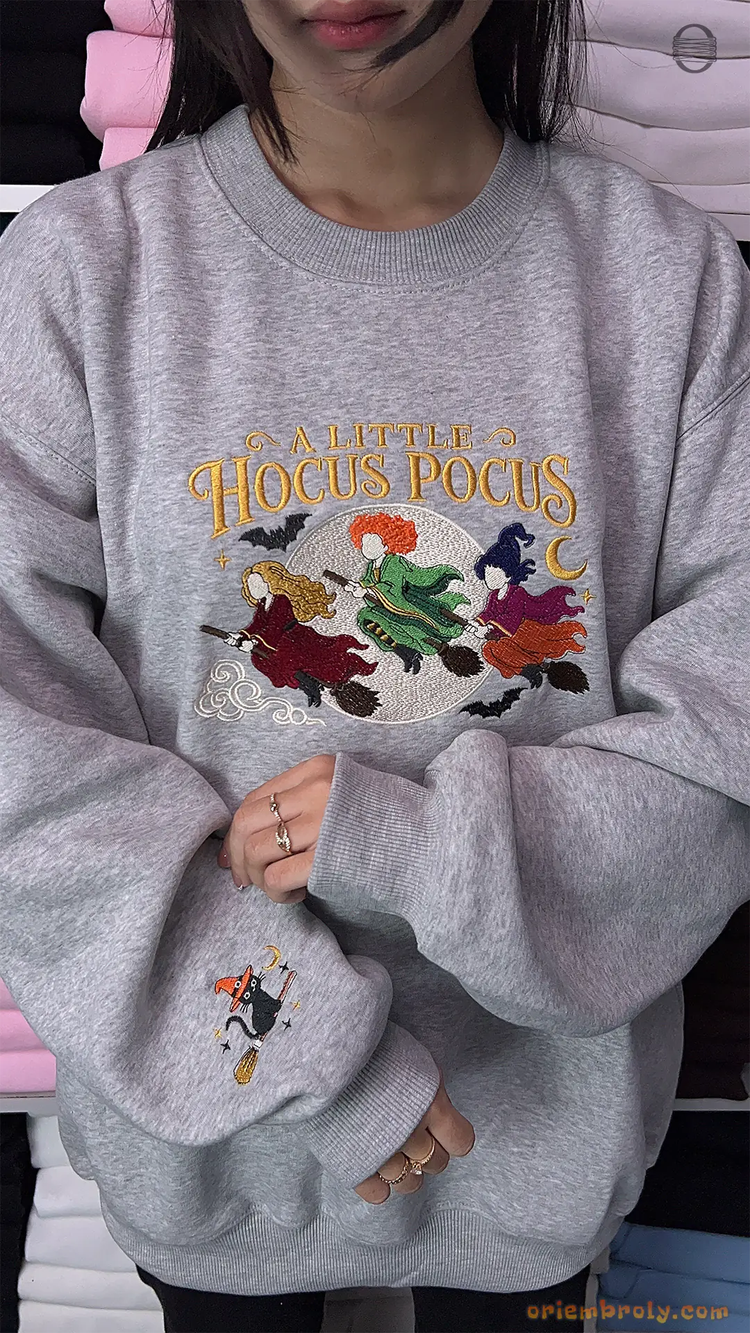 Model wearing a cozy ash gray A Little Hocus Pocus embroidered crewneck sweatshirt with sleeve embroidery indoors.