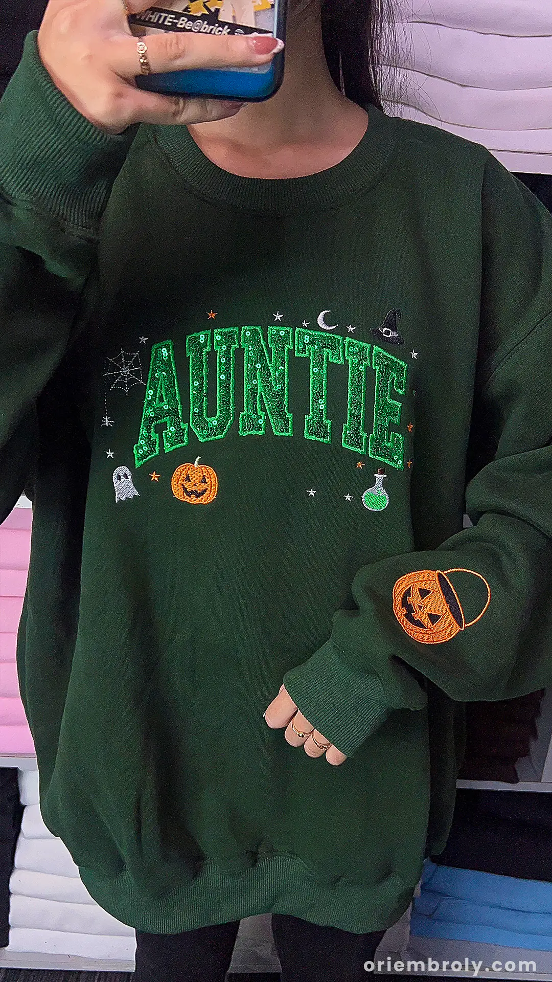 Model wearing a cozy green Auntie Halloween sweatshirt with green sequin inner text and pumpkin sleeve print.