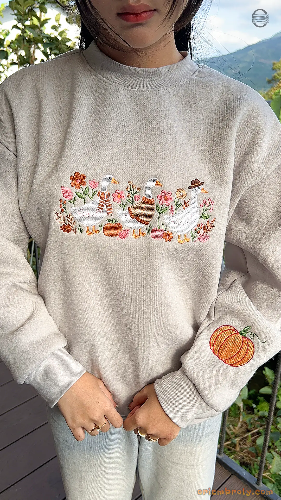 Model showcasing a cozy oatmeal embroidered duck sweatshirt in an outdoor fall setting.