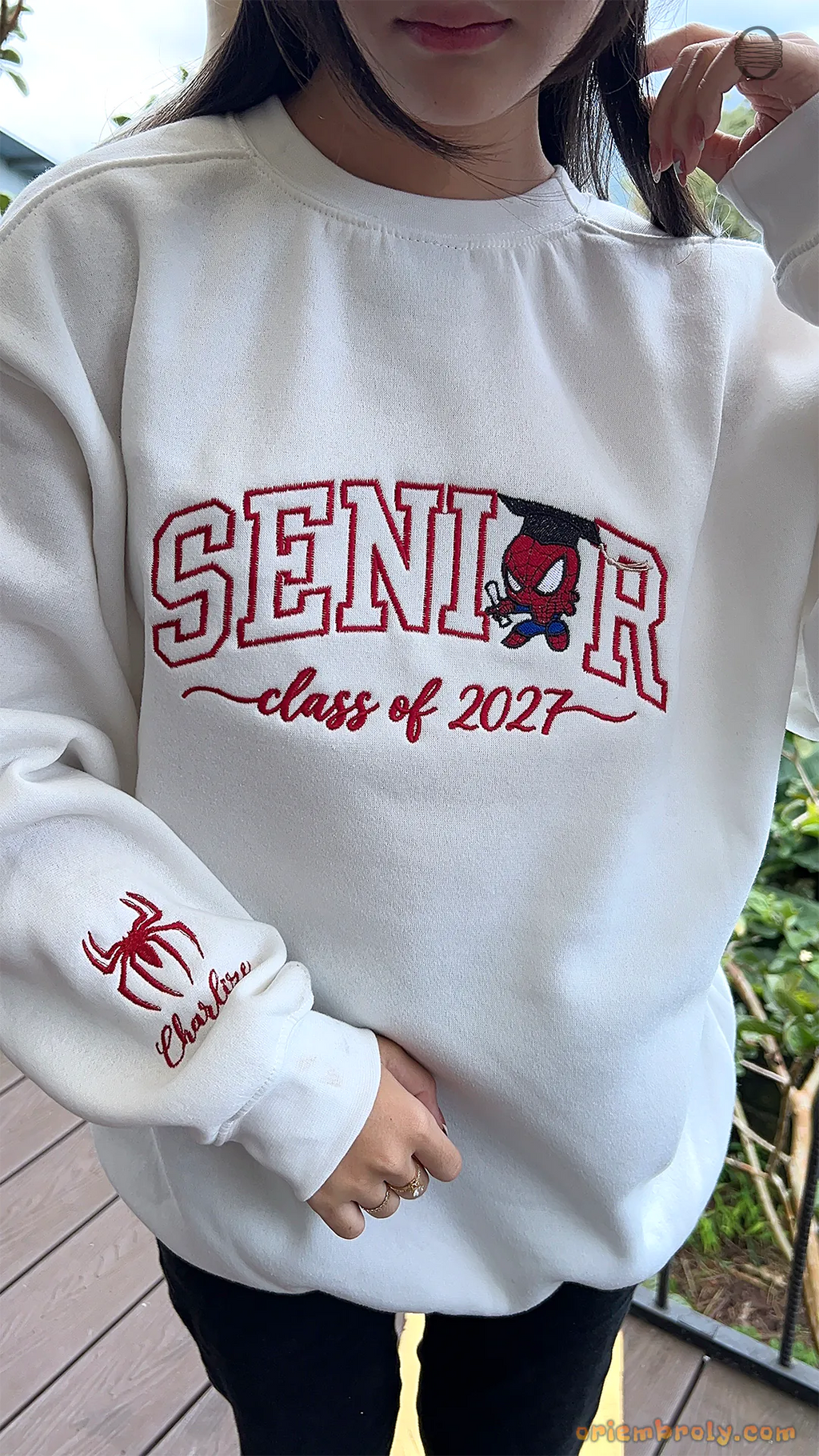 Model showcasing a white Senior Class of 2027 Spider-Man embroidered pullover in an outdoor setting.
