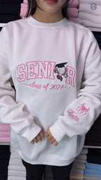 Model posing in a white Senior 2027 sweatshirt showing the custom Spider-Man name embroidery on the sleeve cuff.