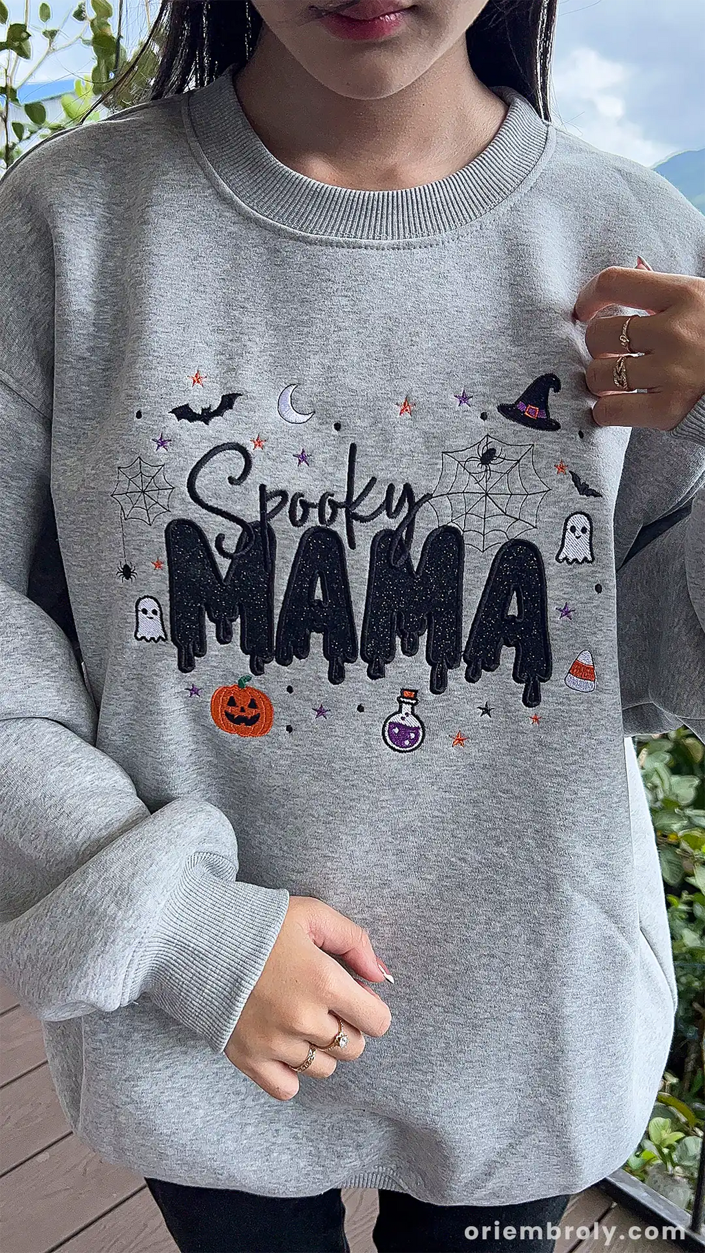Model showcasing a gray Spooky MAMA Halloween crewneck sweatshirt in an outdoor fall setting.
