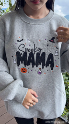 Model showcasing a gray Spooky MAMA Halloween crewneck sweatshirt in an outdoor fall setting.