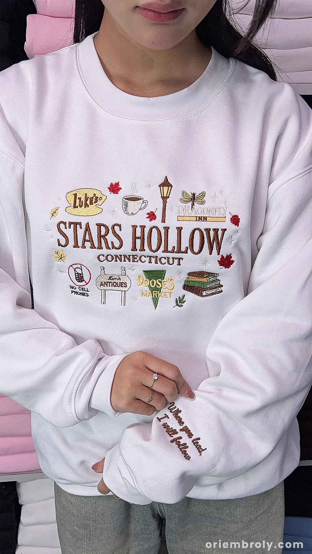 Model wearing a white Stars Hollow Connecticut embroidered crewneck sweatshirt with sleeve detail indoors.
