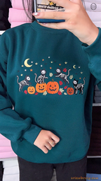 Close-up of a model wearing a cozy teal crewneck sweatshirt with festive skeleton cats and pumpkin embroidery.