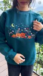 Model showcasing a dark teal skeleton cats and pumpkin embroidered Halloween sweater in an outdoor fall setting