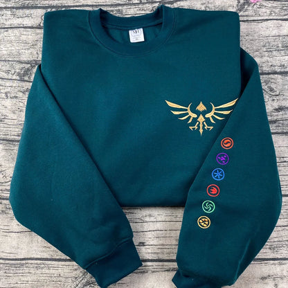 Teal sweatshirt with gold emblem and colorful symbols on a wooden surface